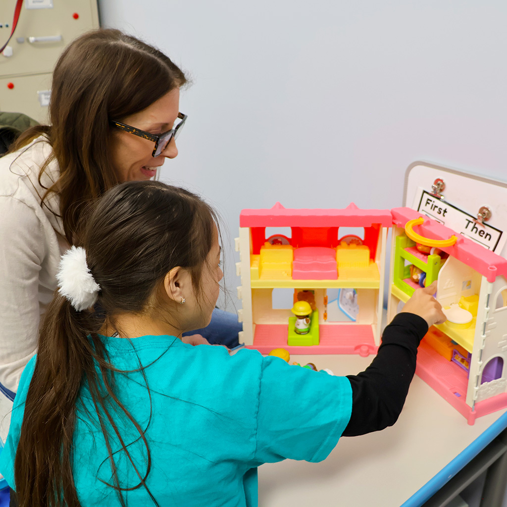 A woman and a girl play with a dollhouse together.