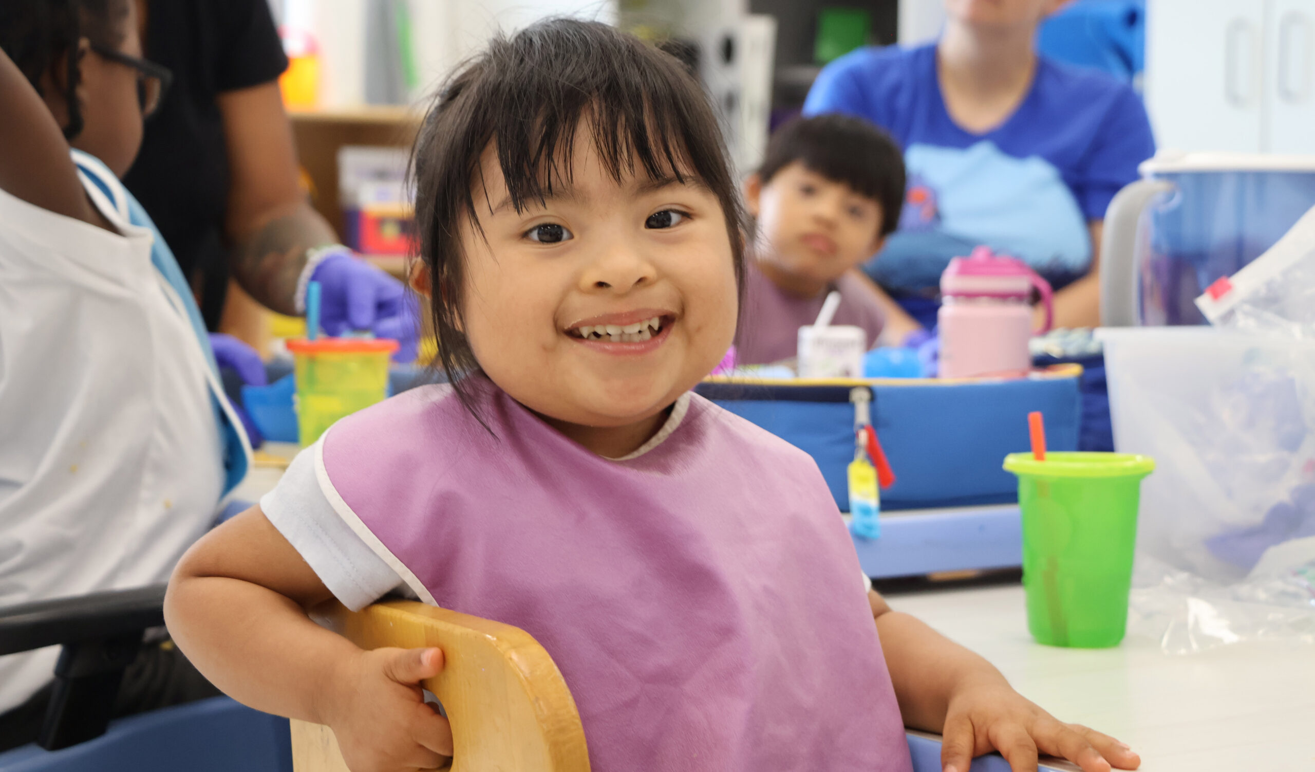 A little girl smiling while wearing a bib and sitting at a lunch table